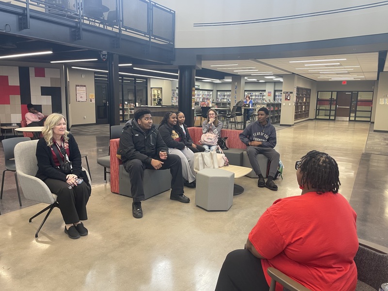 English teacher sitting in chair with her class while Royston sit in chair in front of them speaking to them about books