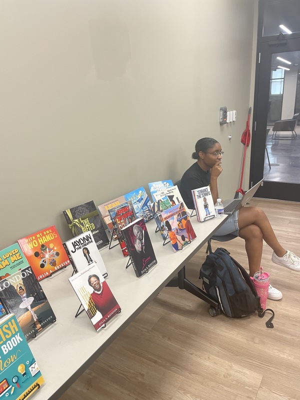 Student sitting in back of room listening next to display table of books
