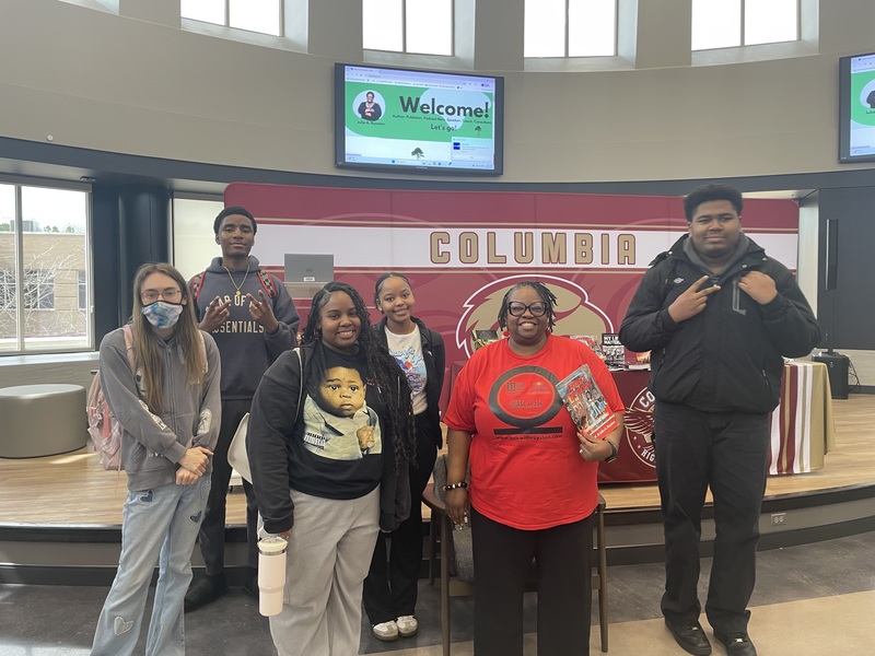 Dr. Royston standing while holdiing a book with 5 students in front of Columbia stage
