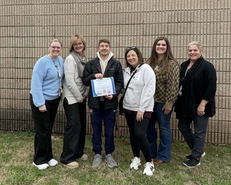 Coach Meadows surrounded by leadership team and community members as he holds his award
