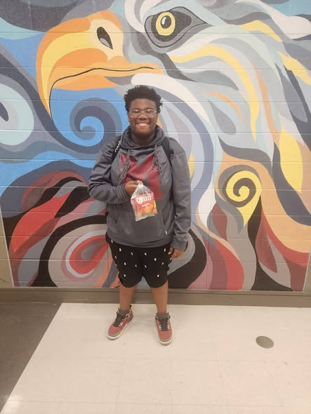 A young man stands in front of an eagle mural holding a goody bag.