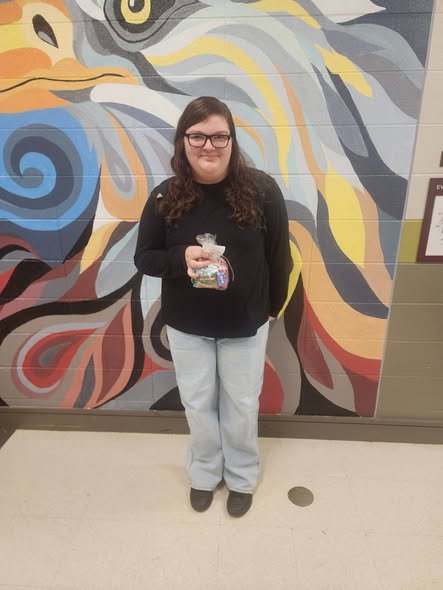 A girl stands in from of an eagle mural holding a goody bag. 