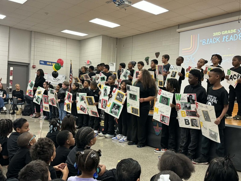 Third grade students on stage performing "Black Leaders" with each student holding a hand-made poster of the leader they were mentioning. 
