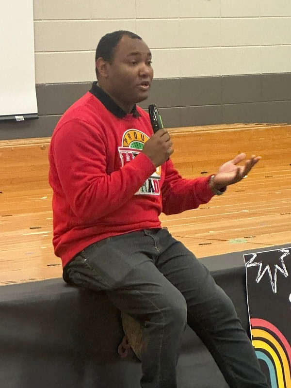 Fox54 News Sports Director, Mo Carter, speaking to the students while sitting on the stage.