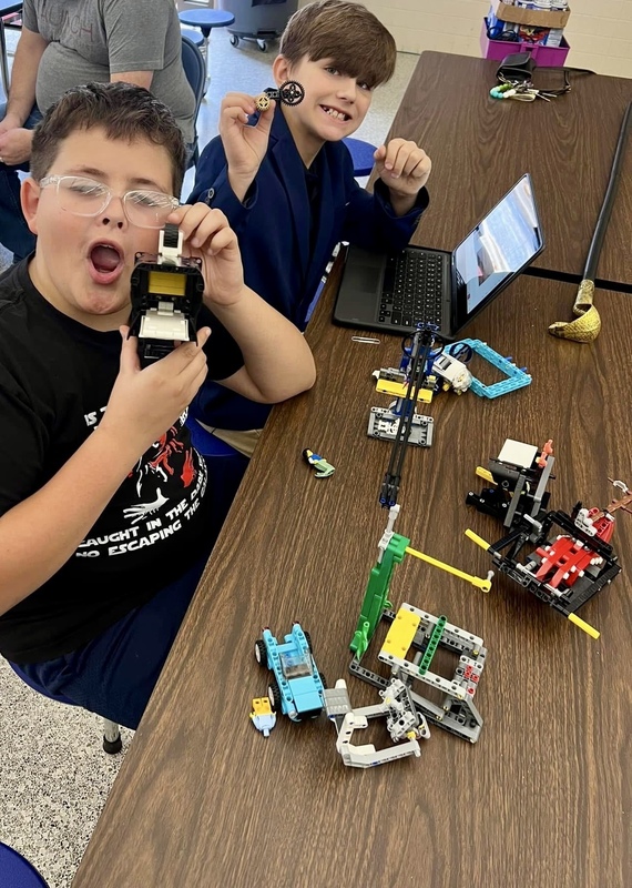 Two boys looking surprised while they hold up robots for the camera