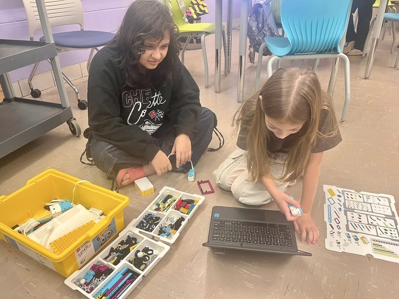 Two female students working with a computer and robotic parts