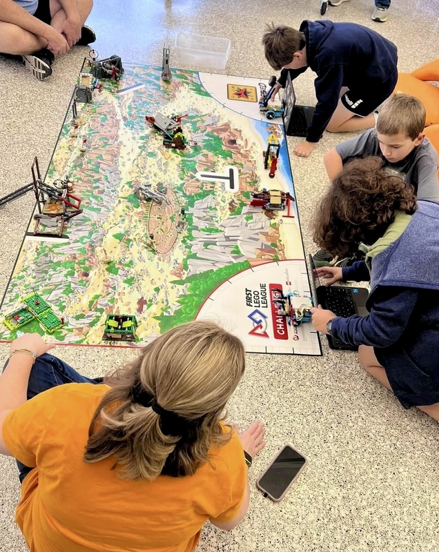 Group of five students work on the floor to construct parts across a map
