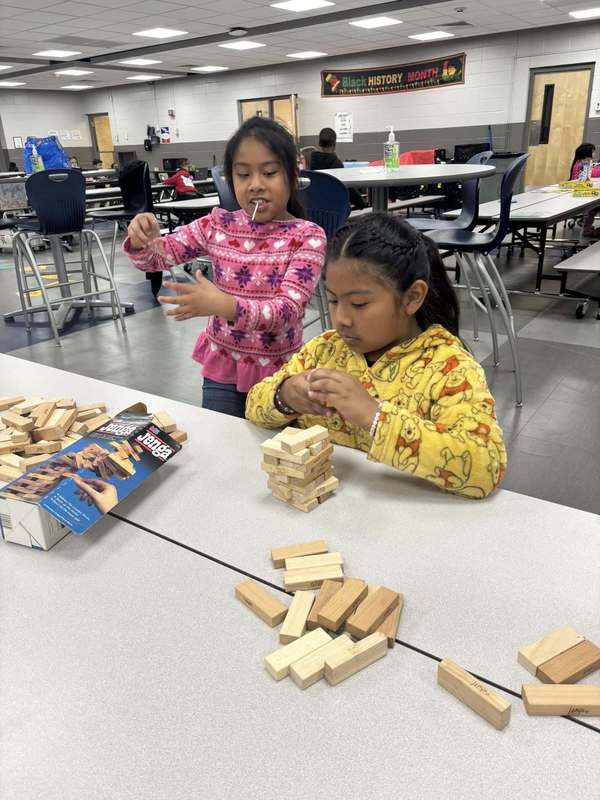 Two second graders stacking a Jenga set before they can play. 