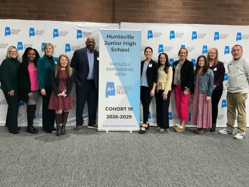 Huntsville Junior  school staff pose with district staff in front of the A+ College Ready Cohort 19 2026-2029 banner