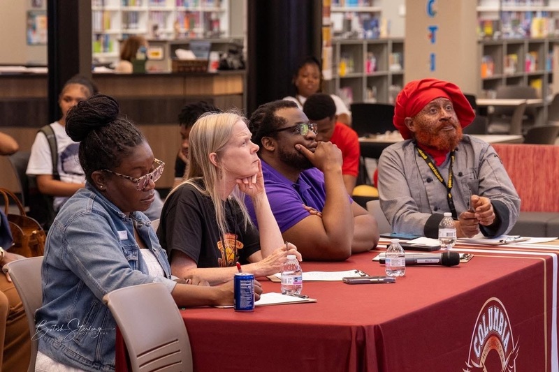 4 judges sitting at table with red cloth with  Columbia logo in front looking ahead