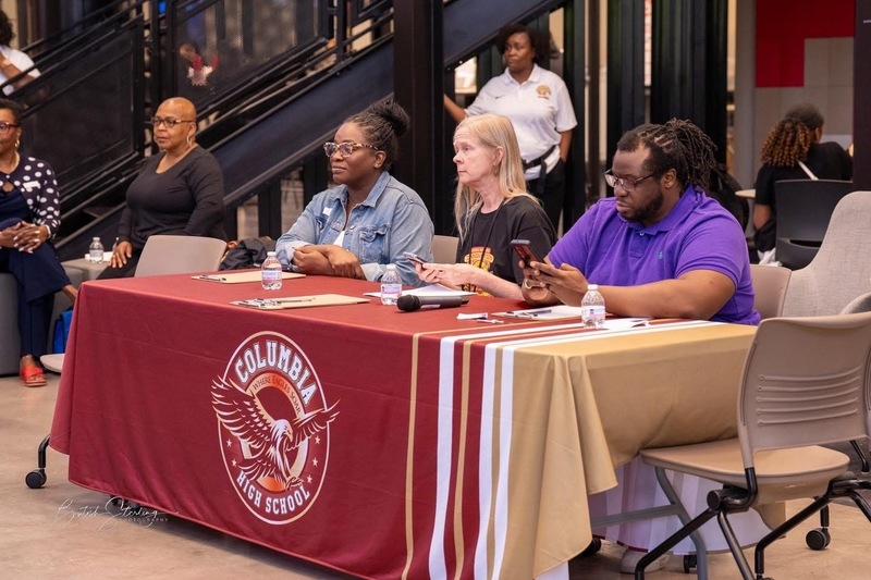 4 people sitting at table with crimson, gold and white table cloth with Columbia logo with eagle on front
