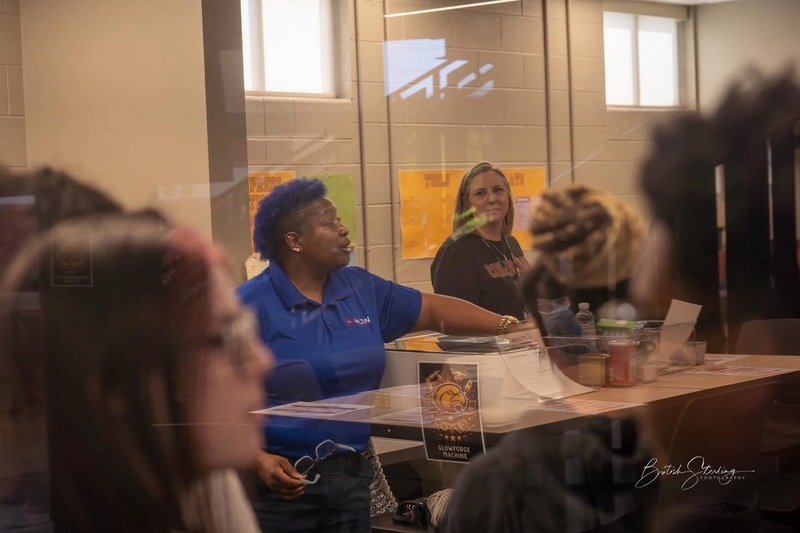 Bonnie, STEM Coordinator with blue shirt and green hair can be seen through glass talking to students