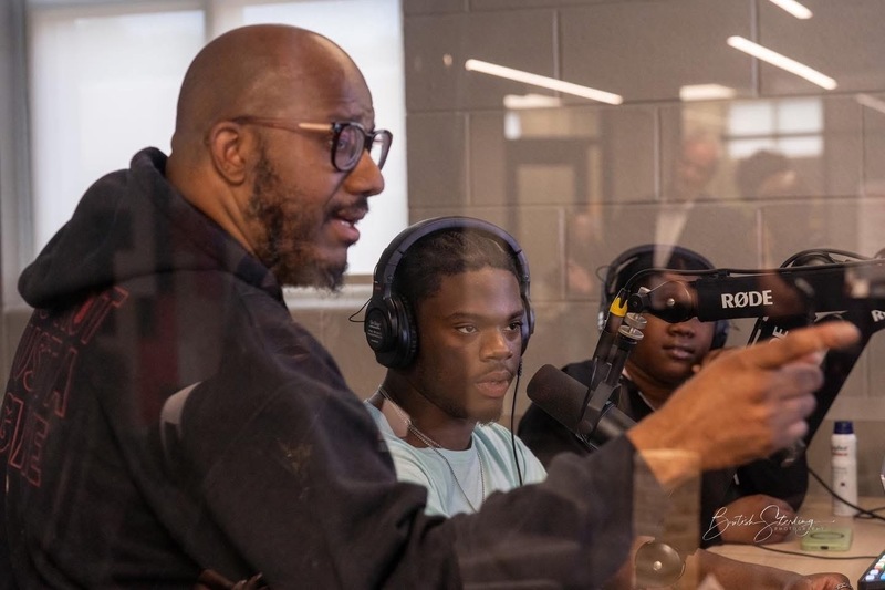 Mr. Merriweather   can be seen through the window of the Podcast room demonstrating to two students