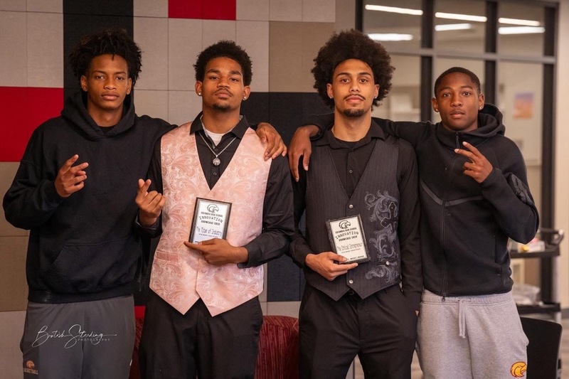 4 students standing, posing for picture while the two students in the middle hold up plagues