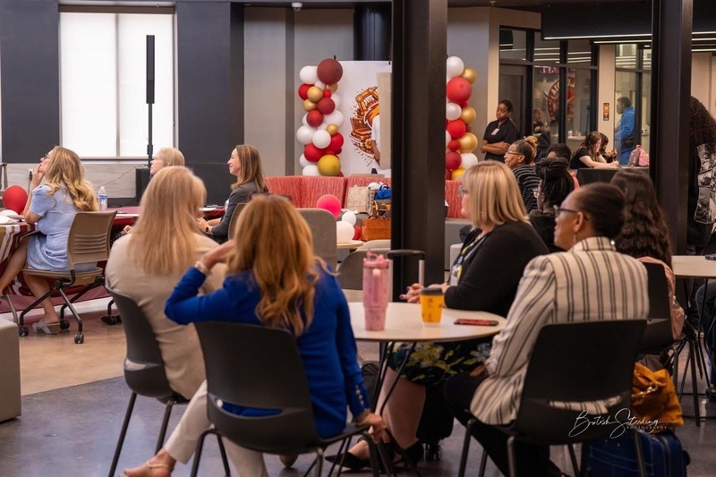 4 women sitting around round table with two black columns, balloon arch in front of them