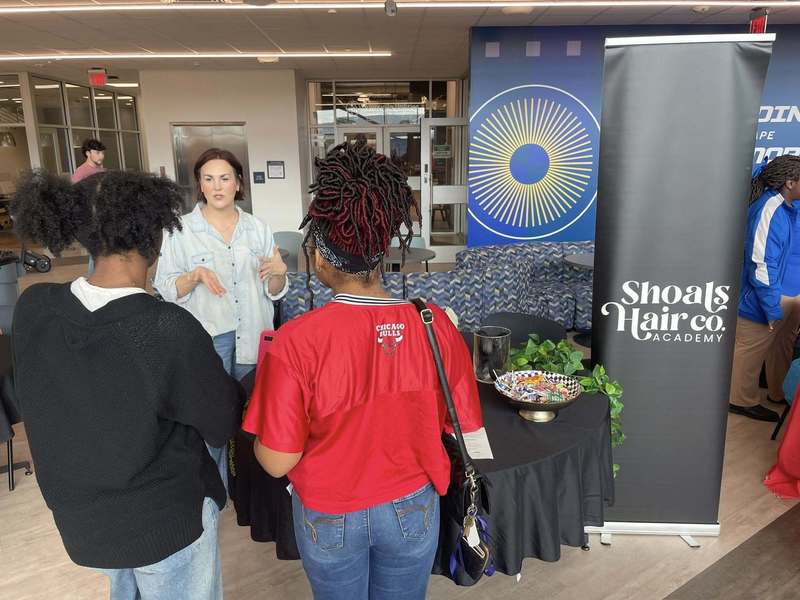 Students speak with a woman from Shoals Hair co. Academy
