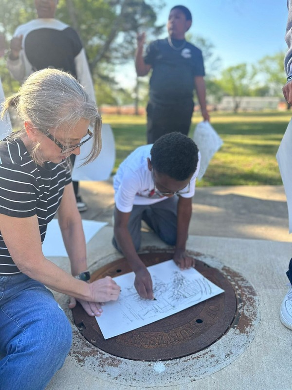 Ms. Darla using a manhole cover to help a student create art during their Painting Club.