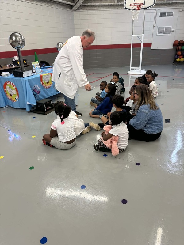 First grade students sitting in the gym listening to the Nutty Scientist about the Van Da Graff Generator.