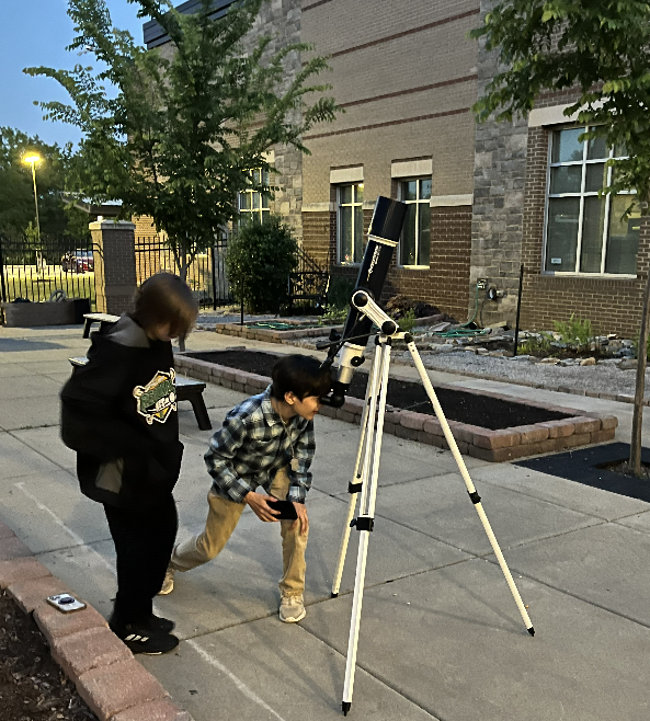 A student waits his turn while another student stoops to checlk out the moon through a telescope
