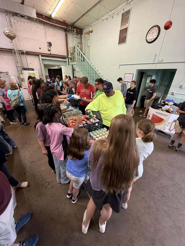 students standing in a serving line serving food to members of homeless community