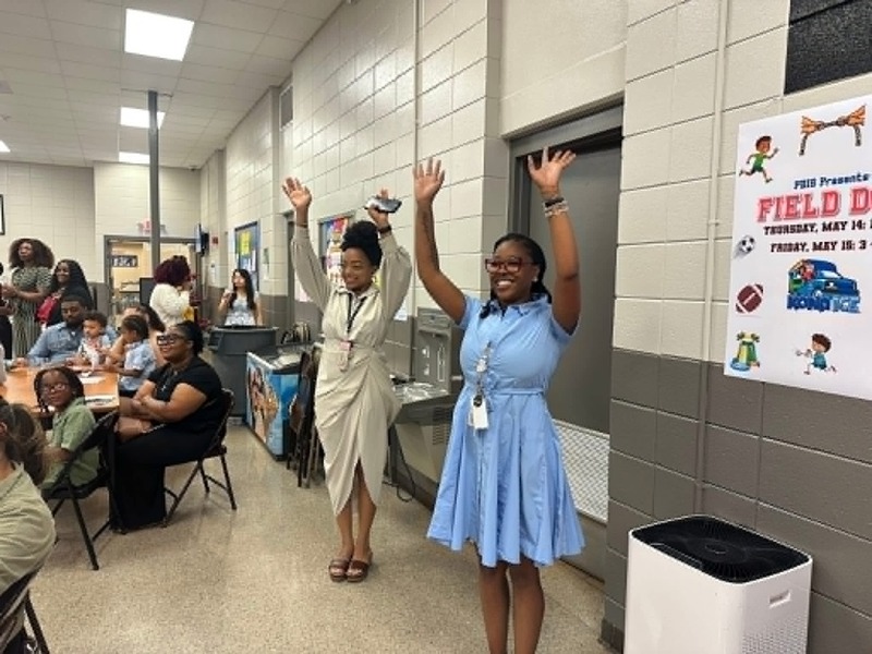 The Pre-K teachers, Mrs. Alexus and Ms. Kiara, on the side of the stage showing their students the motions to the dance.