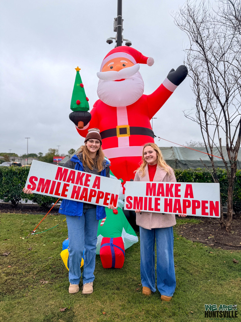 Two Young Women Holding "Make A Smile Happen" signs