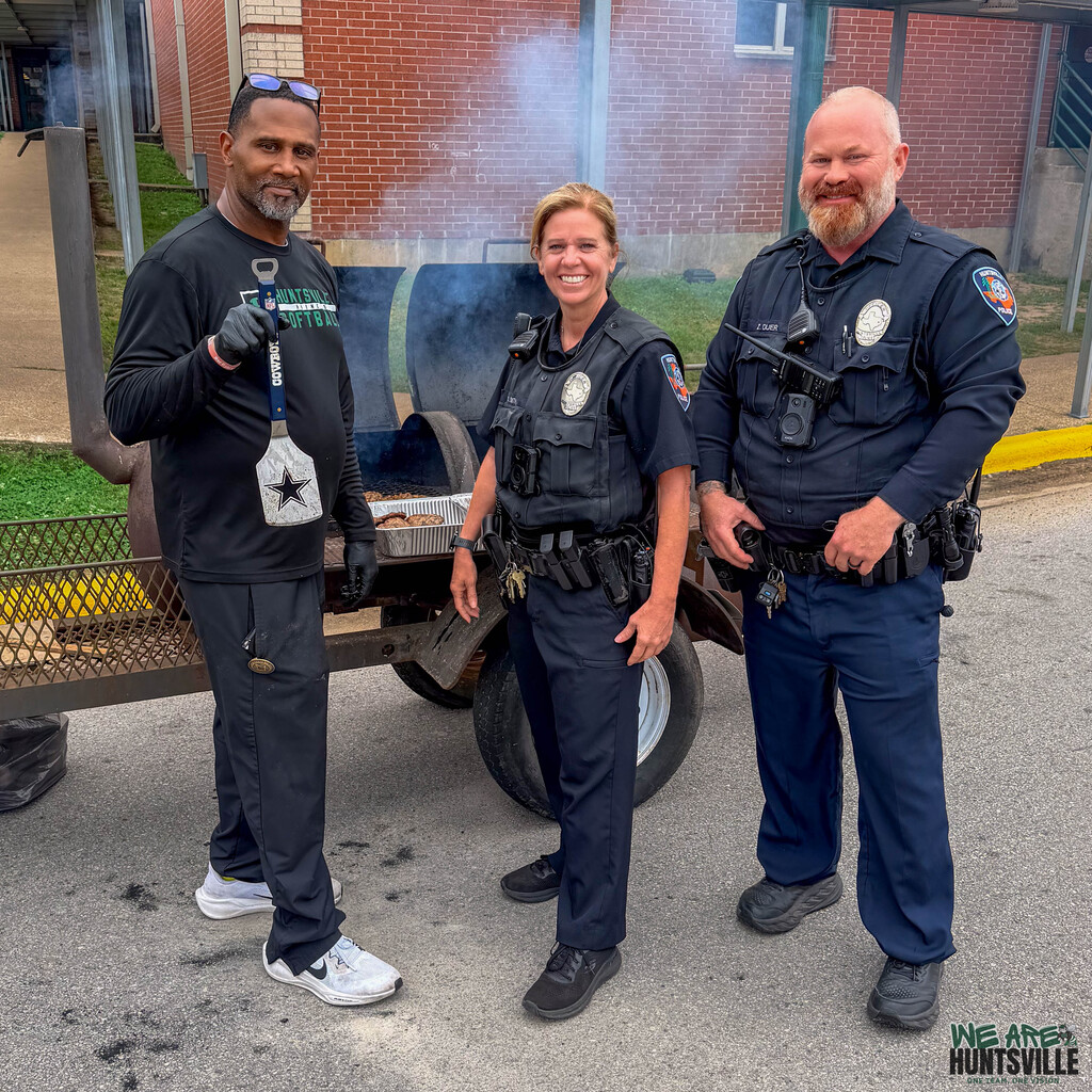Two police officers and a coach in front of a BBQ