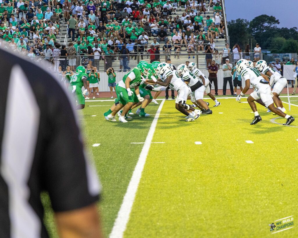 football teams playing on field- with just a touch of the umpire's shirt in the foreground