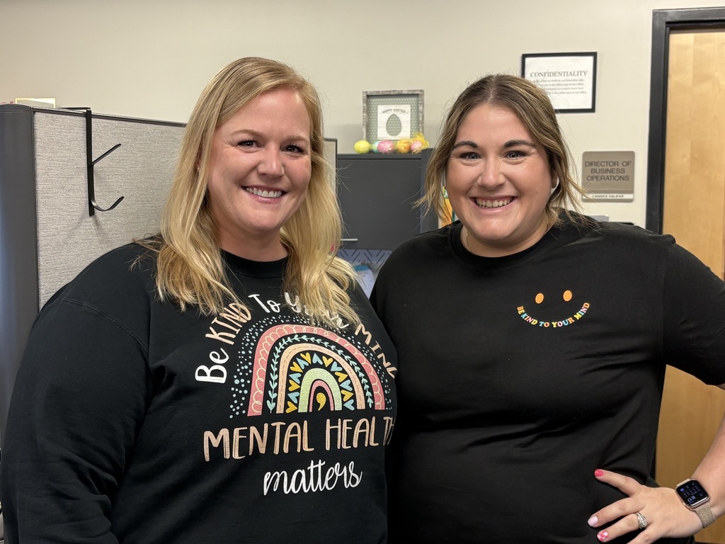 Two educators standing in an office area, smiling and wearing shirts that say “Be Kind to Your Mind” and promote mental health awareness.