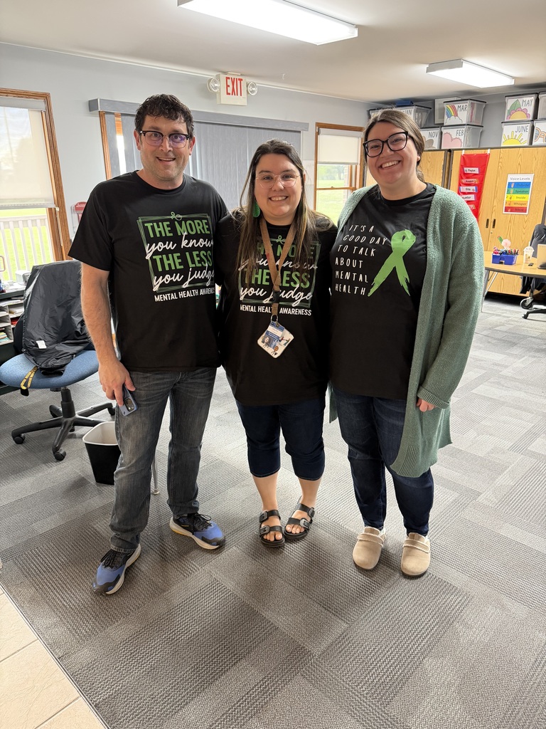 Three educators standing together in a school office or classroom, smiling and wearing black mental health awareness shirts.