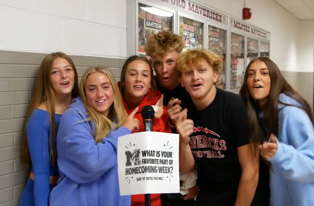Several girls and boys standing in front of a microphone that reads "what's your favorite part of homecoming week?" written on the mic stand