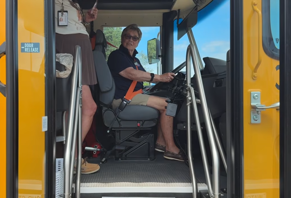 Photo of a woman sitting in a  school bis driver seat with the door open