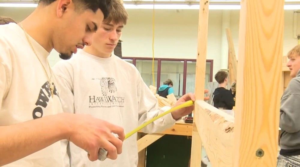 Two male students measuring peieces of wood with a tape measure
