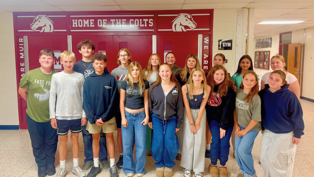 A group photo of student LACES in front of the Muir doors that say Home of the Colts