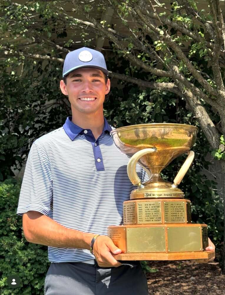 Photo of golfer holding large trophy while smiling and posing