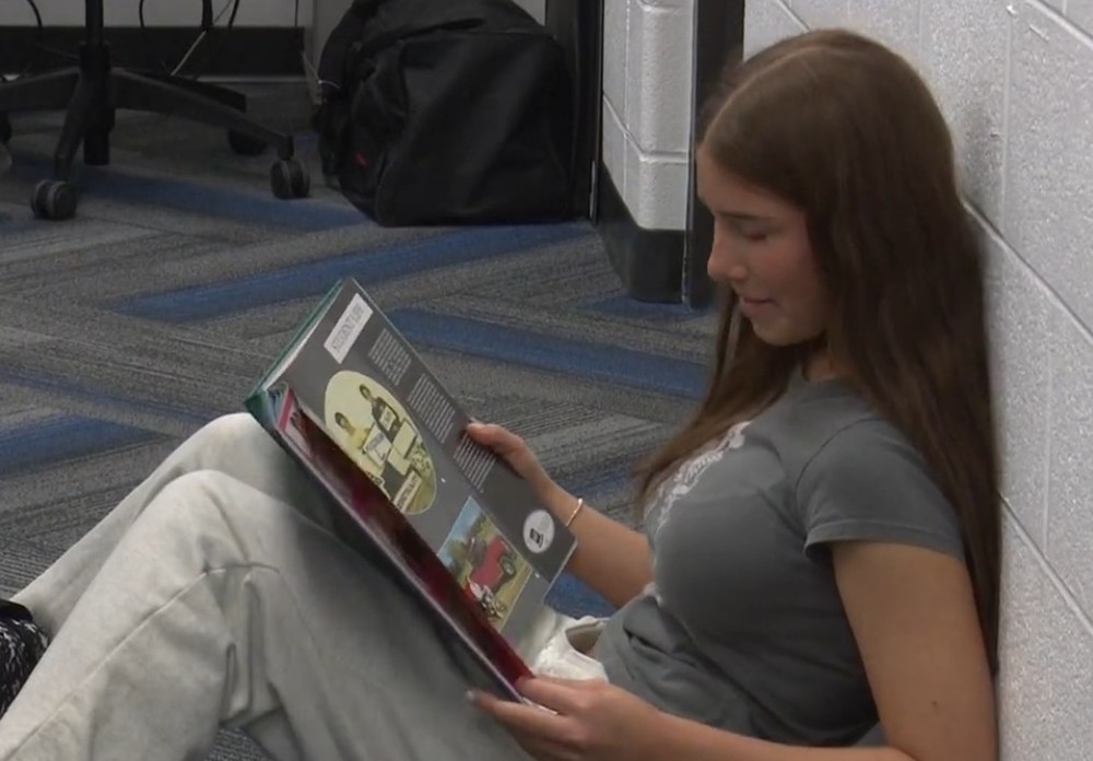 Student sitting on the floor in class flipping through a yearbook