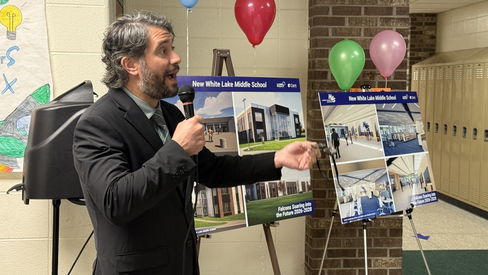 photo of supt. salah talkign on microphone in front of renderings of the renovations at white lake middle school 