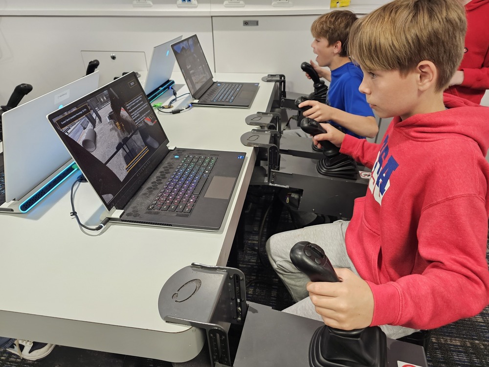 Two young students using joysticks and laptops to drive robot