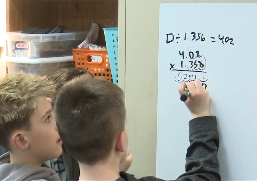 Two boys writing  out math problems on a dry erase board