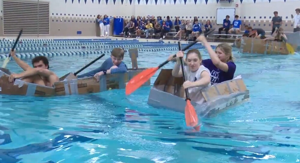 Students in cardboard boats in pool racing 