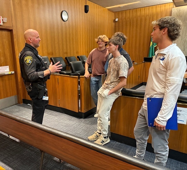 A sheriff deputy talking to a group of students in a courtroom