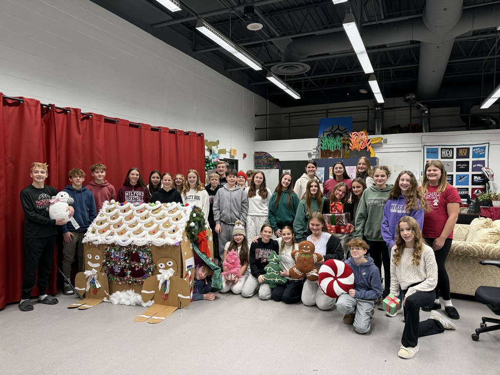 Muir WEB students posing in front of a kid sized gingerbread house