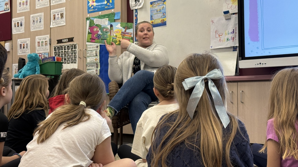 students sitting on the ground listening to teacher read book 