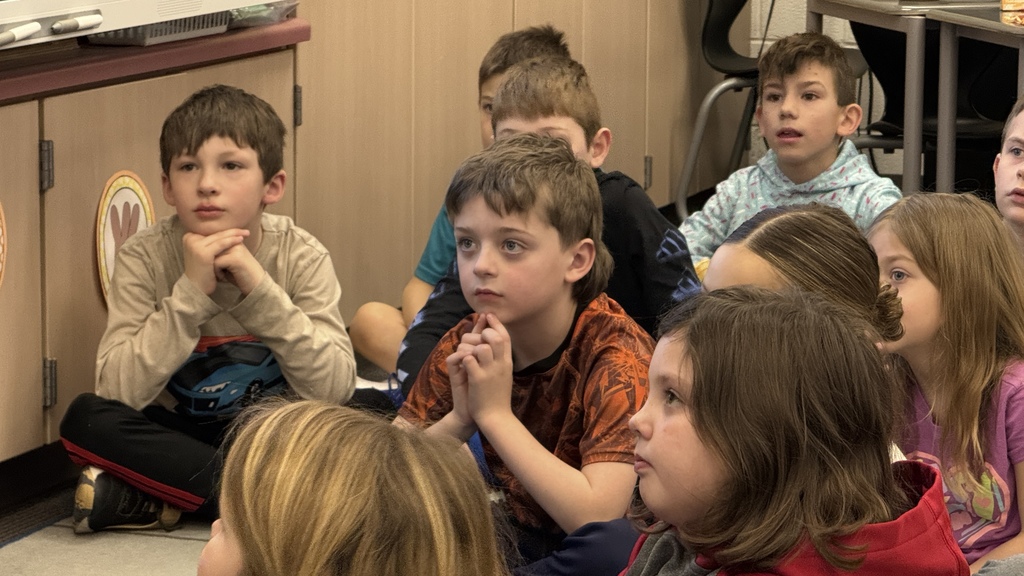 students sitting on the ground listening to teacher read book 