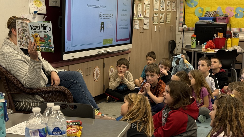 students sitting on the ground listening to teacher read book 