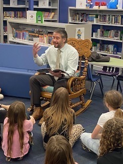 Picture of Supt. Paul Salah reading to 4th Graders from Johnson Elementary who are seated on the floor listening