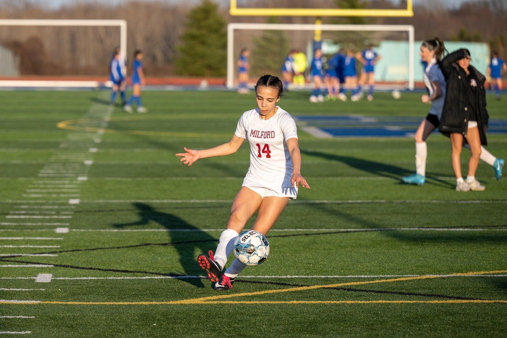 Milford girls soccer player with the kicking a ball 