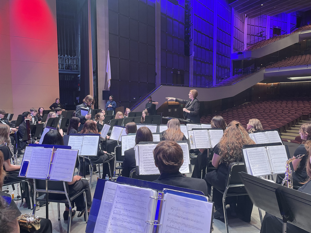 Photo of school band playing on stage being conducted