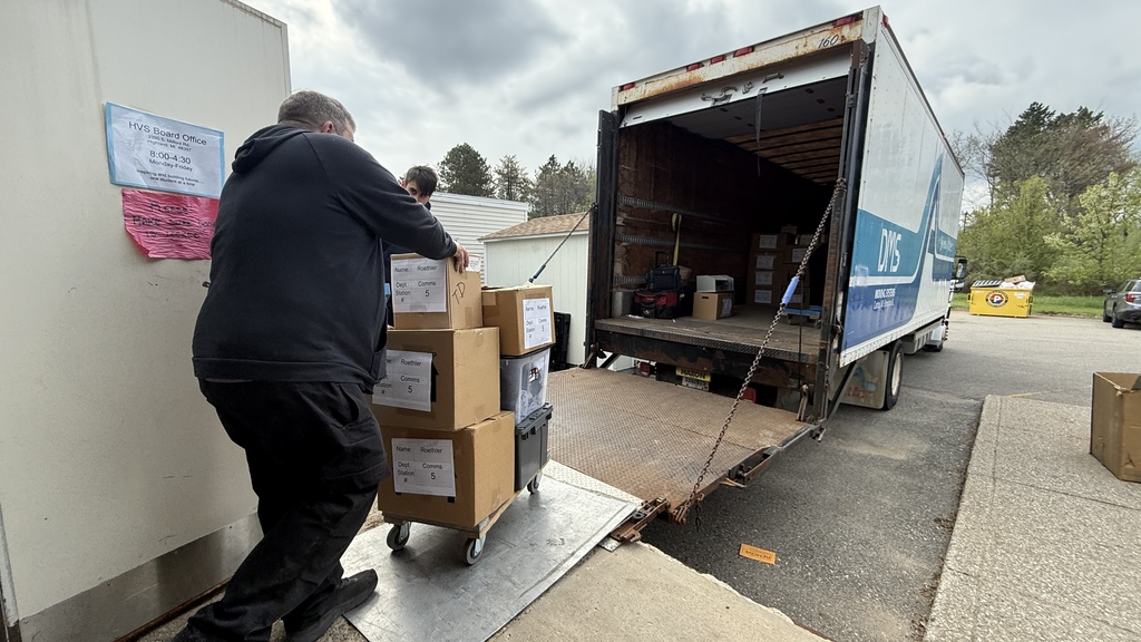 Photo of man pushing cart with boxes on it up onto a large moving truck 