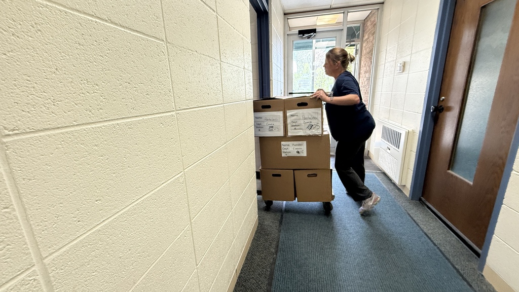 Photo of woman pushing cart with boxes on it down a hallway